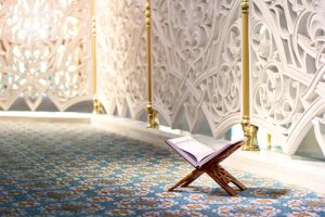 An open Quran on a wooden stand in a mosque with intricate wall designs.