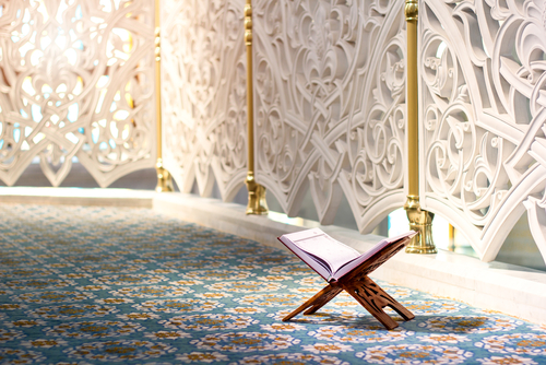 An open Quran on a wooden stand in a mosque with intricate wall designs.