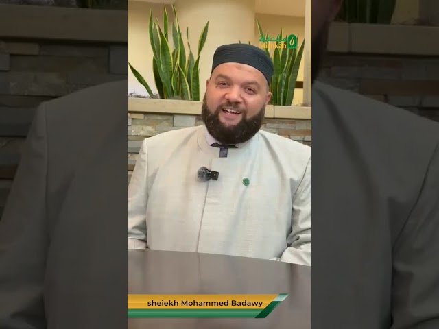 Man in traditional attire smiling indoors with plants in the background.